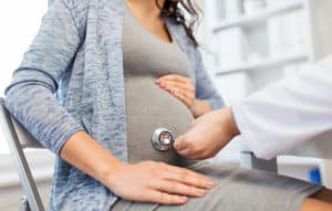 doctor with stethoscope listening to pregnant woman baby heartbeat