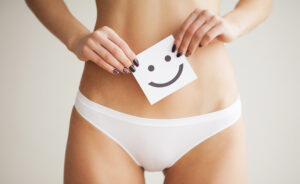 A close-up shot of a woman wearing white underwear holding a card with a smiley face