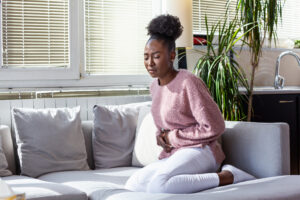 Young woman sitting on her couch and holding her lower abdomen in pain from a pelvic prolapse