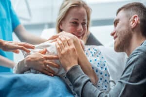 Woman holds her newborn next to her husband at the hospital shortly after her delivery